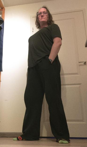 photo of hanneke in wide black sweat pants and a black tee. she has a relaxed but somewhat menacing pose: the photo is taken from almost ground level and hanneke LOOMS